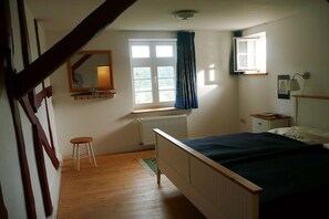 A bedroom with a bed, a window with curtains, a radiator, a nightstand, and a mirror. - Ferienwohnung Kemenate (Trendelburg OT Wülmersen)