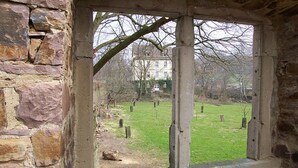 A stone wall with a window revealing a grassy area and a building in the background. - Ferienwohnung Kemenate (Trendelburg OT Wülmersen)