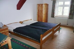 A bedroom with a wooden bed, a wardrobe, a window with curtains, and a bedside table with a lamp. - Ferienwohnung Kemenate (Trendelburg OT Wülmersen)