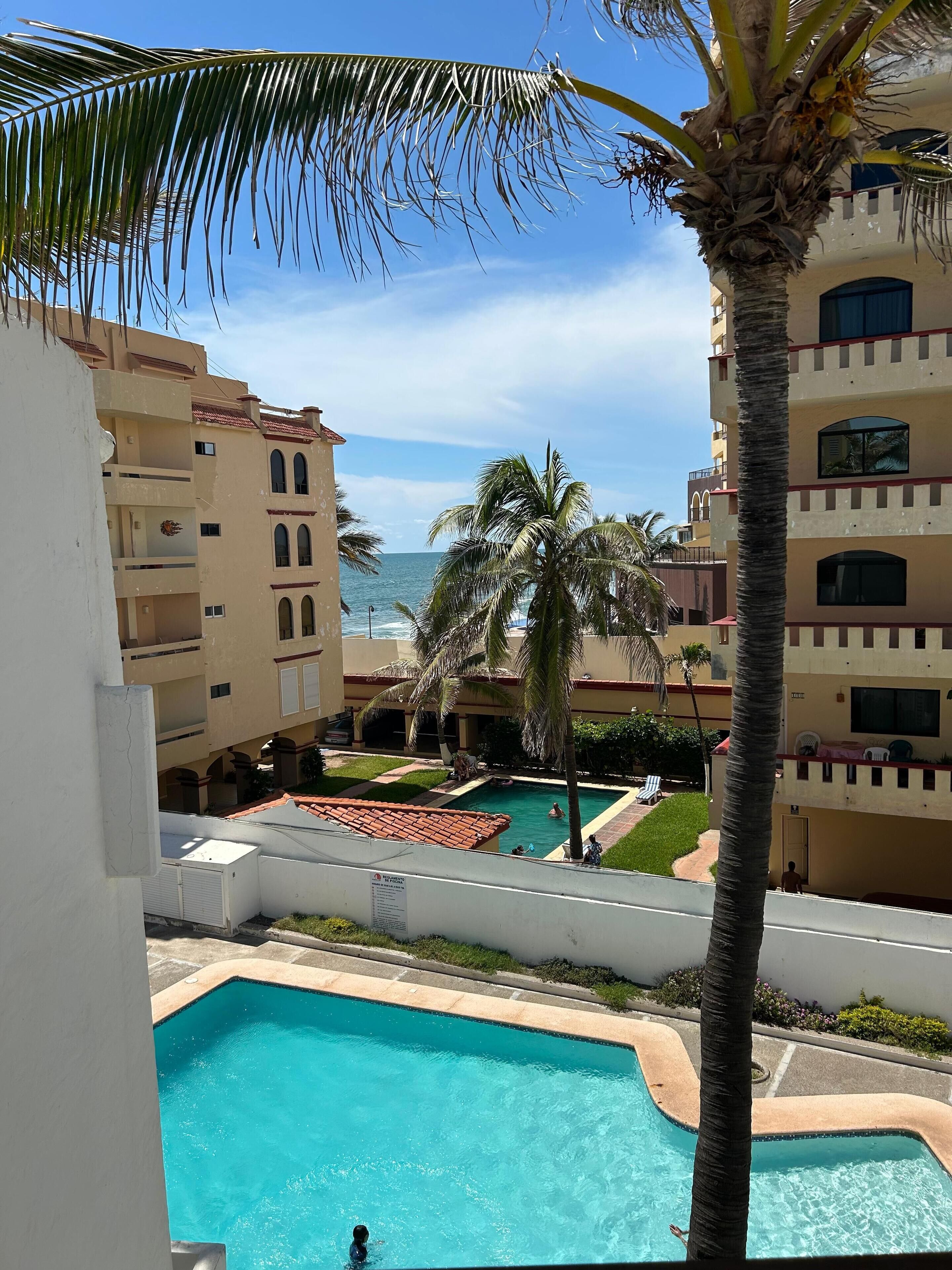 A pool area with a clear view of the ocean, surrounded by multi-story buildings with balconies.