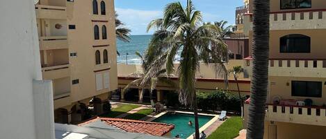 A pool area with a clear view of the ocean, surrounded by multi-story buildings with balconies.