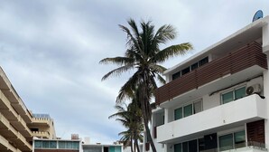 A modern building with multiple floors, a pool area with lounge chairs, and palm trees.