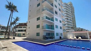 A modern hotel with a pool area, multiple balconies, and a clear blue sky. - Ocean front resort 2-bedroom condo in charming Mazatlán with AC, WiFi (Mazatlán)