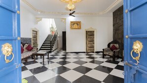 Un sol à carreaux, un escalier, deux fauteuils, un canapé et un lustre.