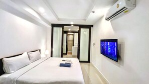 A hotel room with a bed, a TV mounted on the wall, and an air conditioning unit.