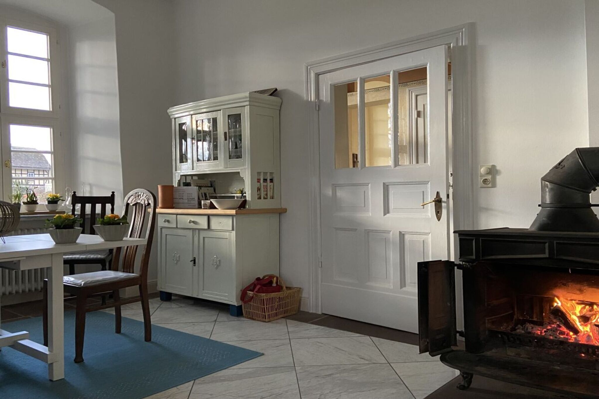 A cozy kitchen with white cabinetry, a dining table with chairs, a fireplace, and a view of the outside through a window.