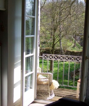 A view from a room with a large window, a wicker chair, and a white metal gate leading to a garden. - Schöne Wohnung in Hessen mit Ruhebereich (Hesse)