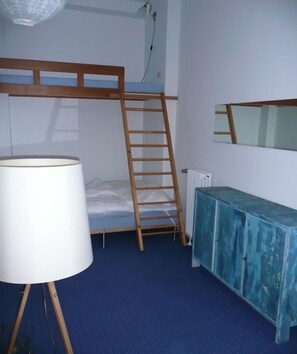 Una cama tipo litera con escalera, una lámpara blanca, un radiador y un armario azul.