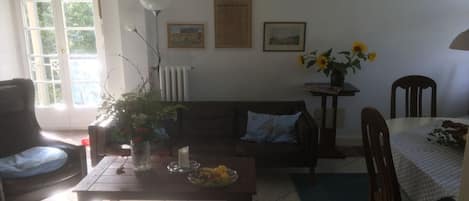 A living room with a sofa, a coffee table with fruit and flowers, a dining table with a chair, and a radiator.