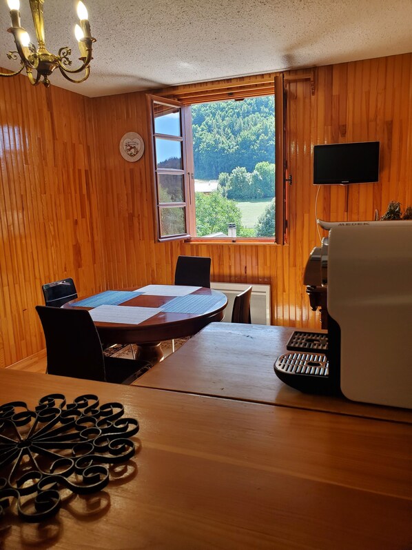 Enjoy a peaceful view of the surrounding landscape from the large window in this room, which features a dining table, TV, and coffee machine.
