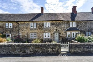 A stone house with a traditional design, featuring a front door, multiple windows, and a small garden area.