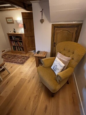 A cozy living room with a plush armchair, a small wooden side table, a bookshelf, and a patterned rug.