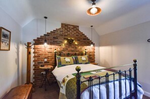 A bedroom with a brick wall, a bed with a quilt, a small stool, and a hanging light fixture.