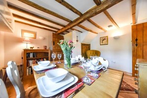 A dining area with a wooden table set for four, surrounded by chairs, with a bookshelf and a vase of flowers on the wall.