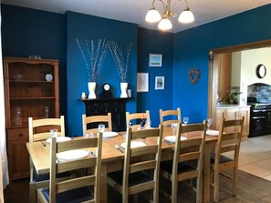 A dining area with a wooden table and chairs, a blue wall, and a kitchen in the background.
