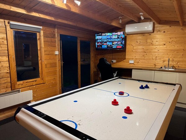 A room with a foosball table, wooden walls, a television displaying multiple channels, and a window.