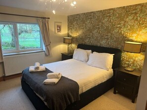A neatly made bed with a dark headboard, two bedside lamps, and a window with curtains.