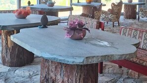 An outdoor seating area with stone tables and benches, surrounded by large windows offering views of the landscape. - Hergül Holiday Village (Gazipasa)