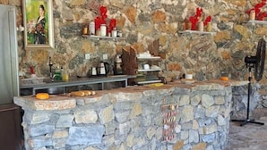 A stone counter with a rustic stone wall backdrop, a fan, and various kitchen items. - Hergül Holiday Village (Gazipasa)