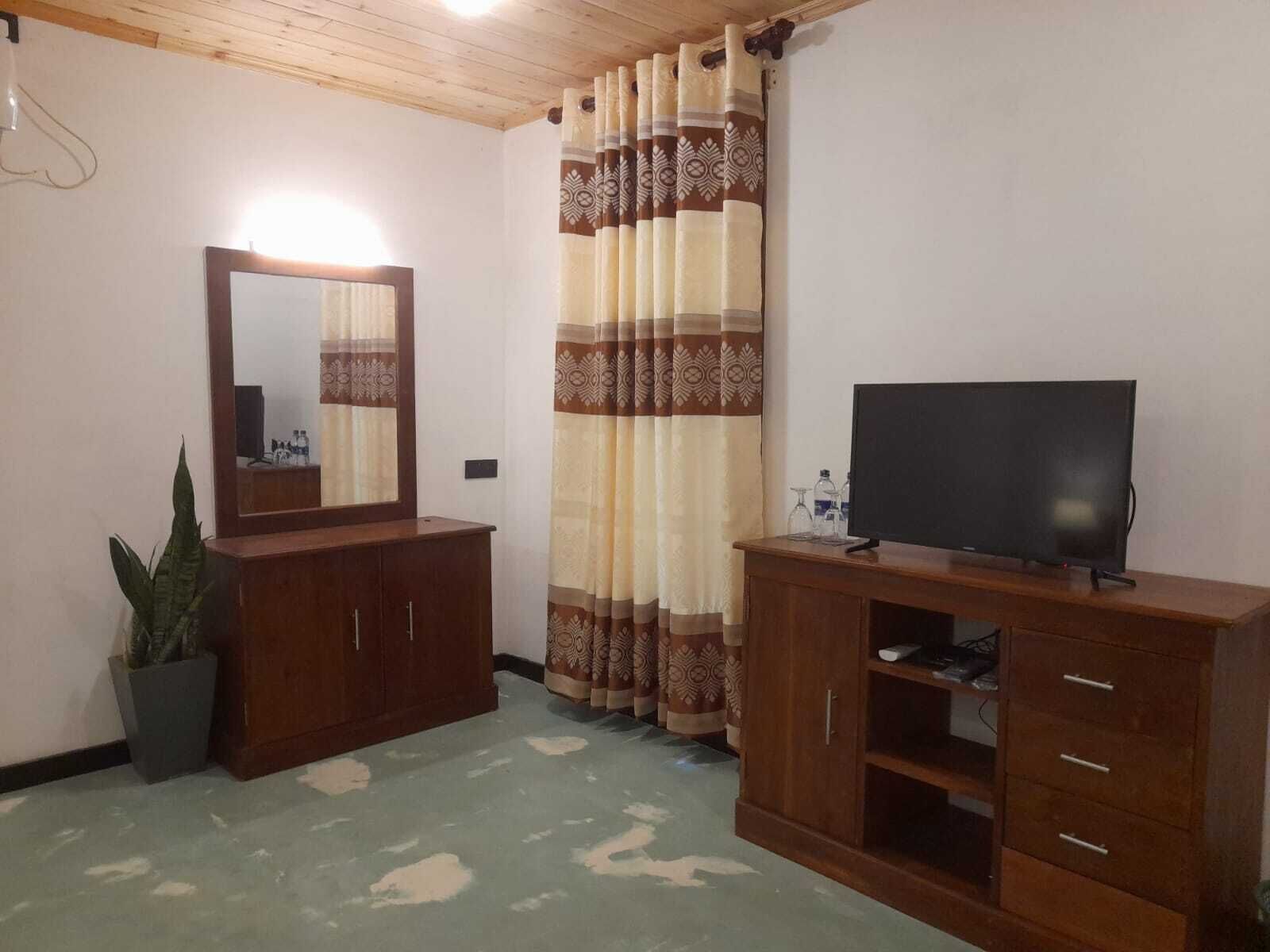 A room with a wooden cabinet, a television on a stand, a mirror, and a patterned curtain.