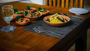 A dining table with multiple dishes, a glass of water, and a wooden chair in a room with a view of greenery. - NATURALIZA (Dambulla)