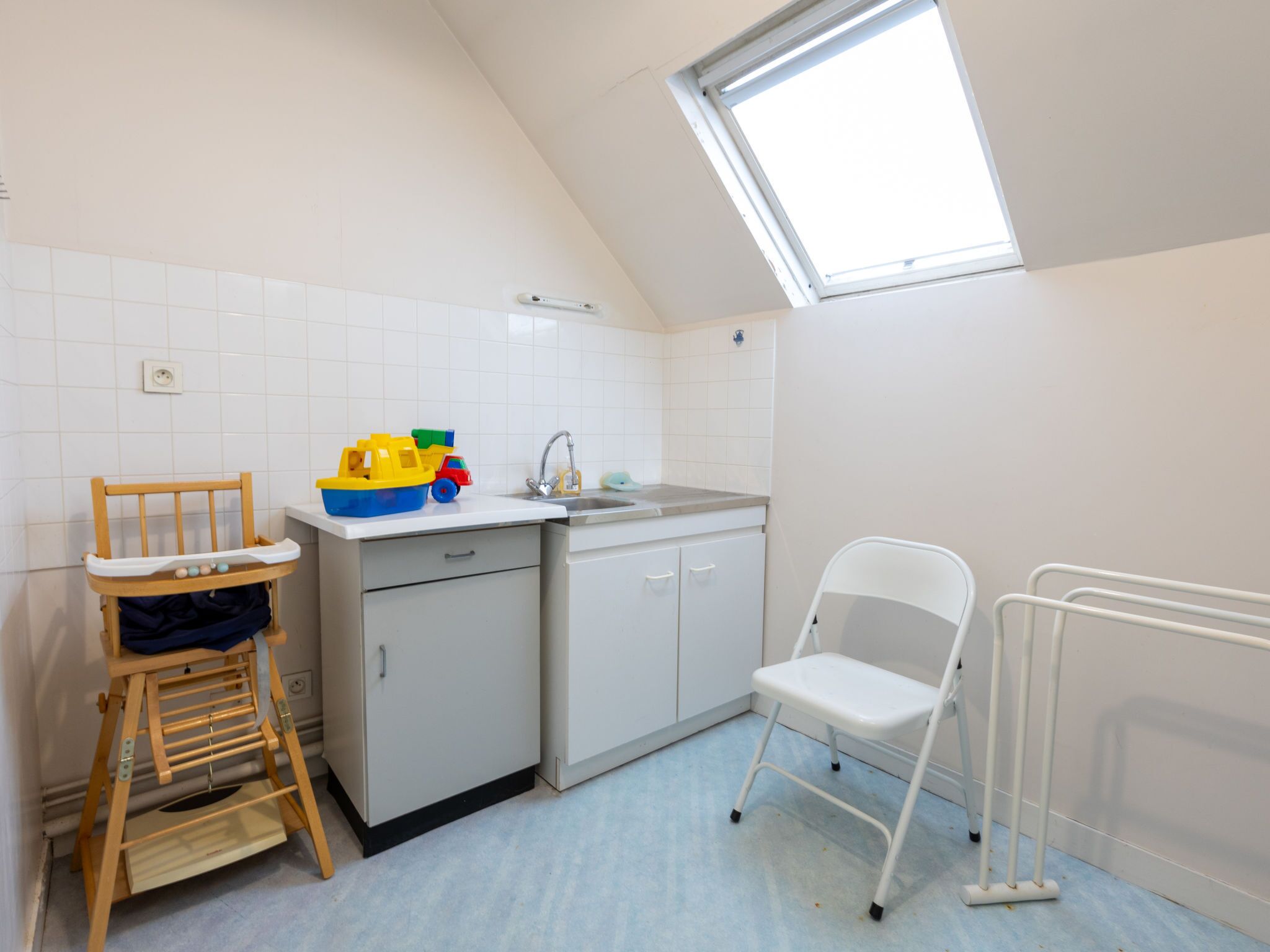 A kitchen with a high ceiling, a skylight, white cabinets, a sink, and a wooden chair.