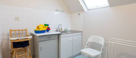 A kitchen with a high ceiling, a skylight, white cabinets, a sink, and a wooden chair.