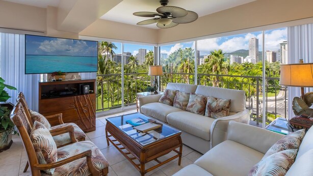 A spacious living room with a large TV, comfortable seating, and a balcony with a city view. - Waikiki Shore 518 Partial Ocean View 2 Bedroom (Honolulu)