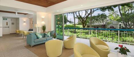 A modern hotel lobby with a large window, a wooden ceiling, and a seating area with yellow chairs.