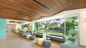 A spacious lobby with a modern design, featuring a wooden ceiling, large windows with a view of greenery, and comfortable seating areas. - Waikiki Shore 518 Partial Ocean View 2 Bedroom (Honolulu)