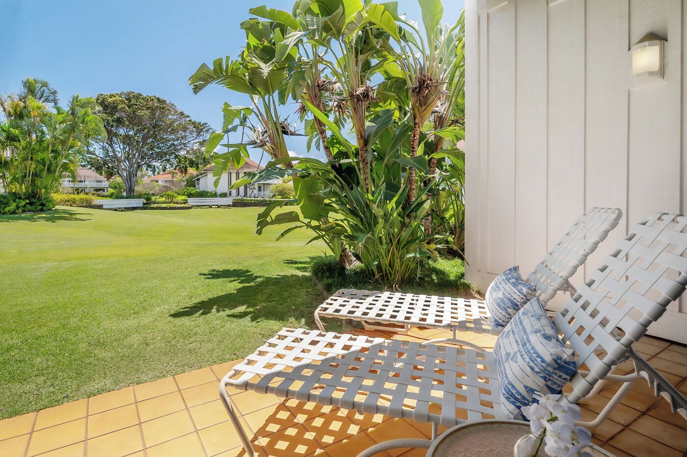 A patio with two white lounge chairs, a small table, and a potted plant.