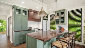 Una cocina moderna con una isla central, taburetes de bar y vistas a la vegetación a través del ventanal.