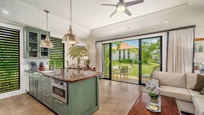Una cocina moderna con una isla central, un comedor con mesa y sillas, un sofá y vistas a un jardín a través de grandes puertas correderas.