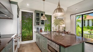 Una cocina moderna con una isla grande, electrodomésticos de acero inoxidable y vistas a un jardín tropical.