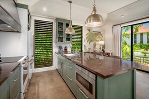Uma cozinha moderna com uma ilha grande, eletrodomésticos de aço inoxidável e vista para um jardim tropical.