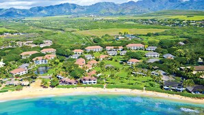 Un complejo turístico frente al mar con varias edificaciones tipo bungalow, una playa y montañas al fondo.