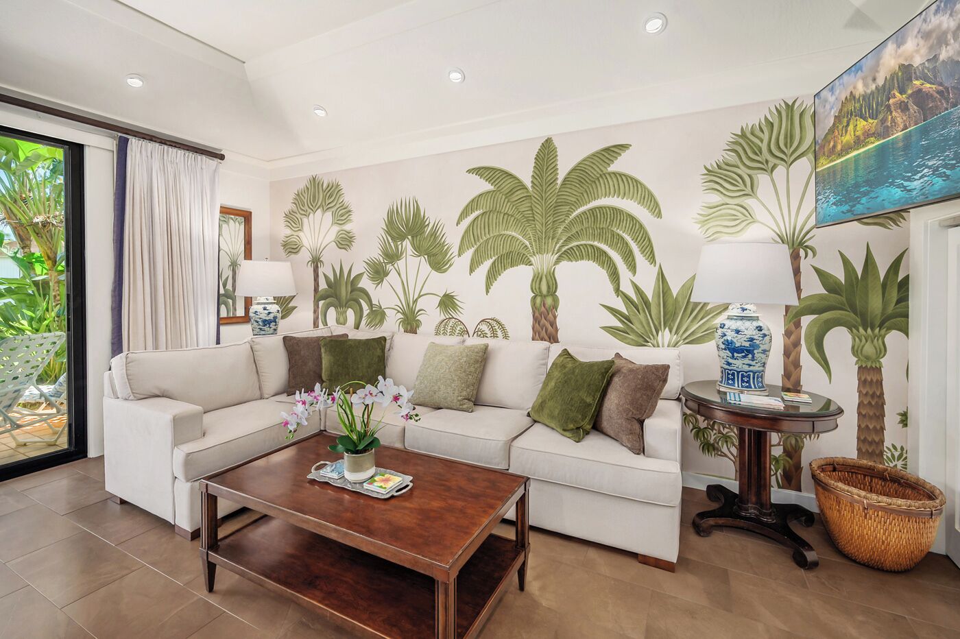 A living room with a white sofa, a wooden coffee table, and a painting of a tropical landscape.