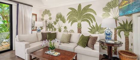 A living room with a white sofa, a wooden coffee table, and a painting of a tropical landscape.