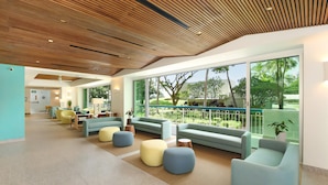 A modern lounge area with seating and a view of a landscaped outdoor area. - Waikiki Shore 1016 Ocean View 1 Bedroom (Honolulu)
