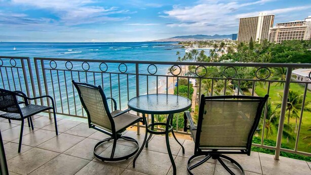 Uma varanda com vista para o oceano, duas cadeiras e uma pequena mesa.