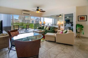 A spacious living area with a glass table, wicker chairs, a green sofa, and a balcony with a city view.