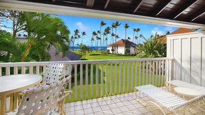 A covered outdoor area with a view of the ocean, palm trees, and a building with a red roof.