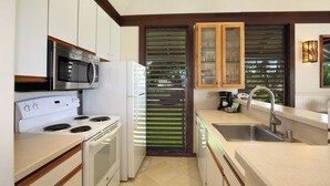 A compact kitchen with a microwave, stove, refrigerator, and a sink.