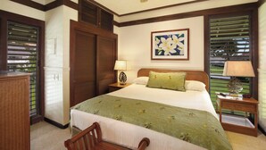 A hotel room with a bed, two bedside lamps, a ceiling fan, a framed floral artwork, and a view through the window blinds.