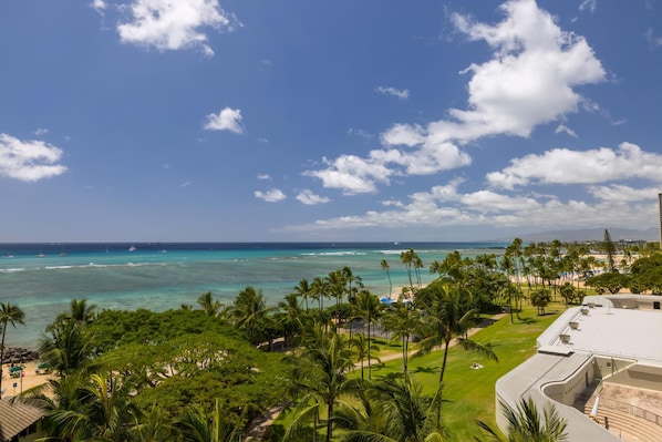A tropical resort with a beach view, palm trees, and a clear sky.