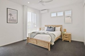 Un dormitorio con cama, mesitas de noche, ventilador de techo y ventana con persianas.