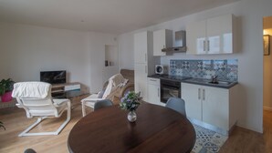 A modern living room with a dining table, a sofa, a TV, and a kitchen area with cabinets and a microwave.