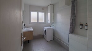 A compact bathroom with a washing machine, a sink, and a shower.
