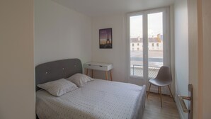 A bedroom with a bed, a desk, a chair, and a window with a view of buildings.