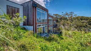 A modern house with large windows, a wooden exterior, and a surrounding natural landscape. - The Peninsula Grande (Karikari Peninsula)